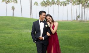 Couple in a tuxedo and burgundy gown on a palm-lined lawn at a destination wedding