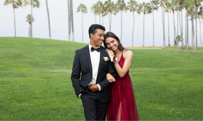 Couple in a tuxedo and burgundy gown on a palm-lined lawn at a destination wedding