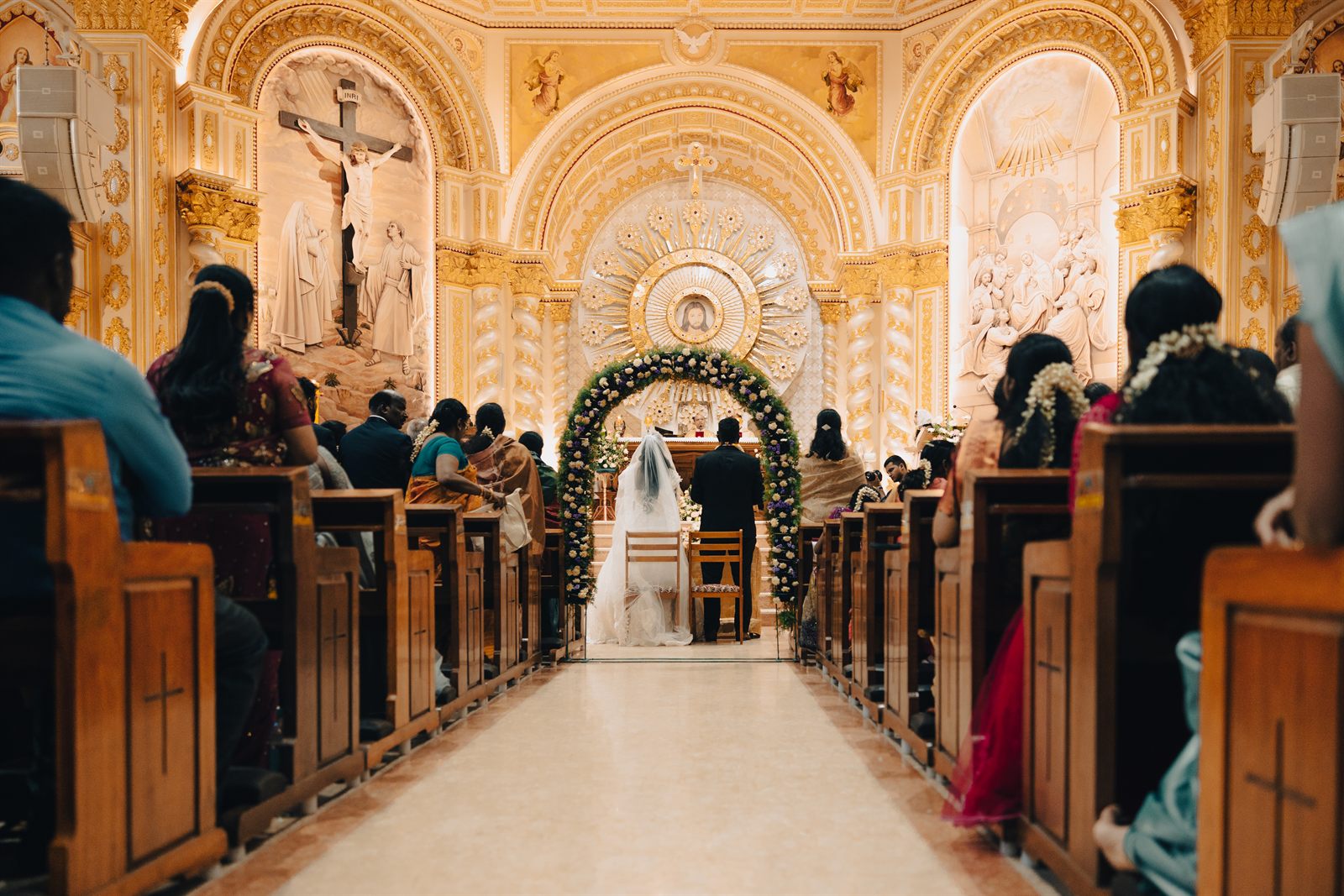 Church wedding ceremony with the couple at a floral arch altar and guests in the pews