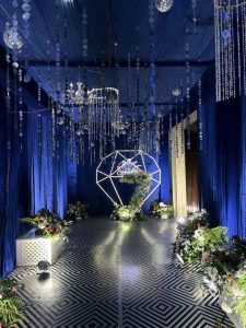 Luxury wedding reception with royal blue drapes, crystal chandeliers and a geometric floral arch