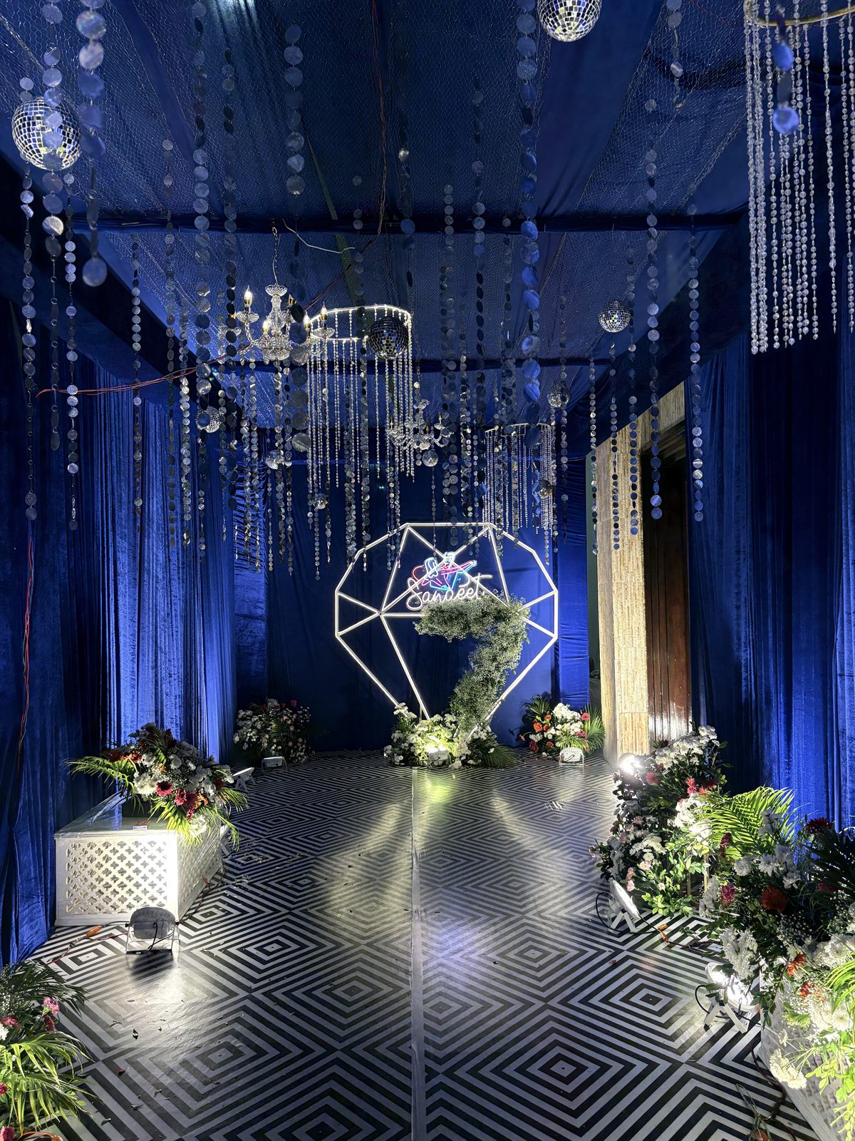 Luxury wedding reception with royal blue drapes, crystal chandeliers and a geometric floral arch