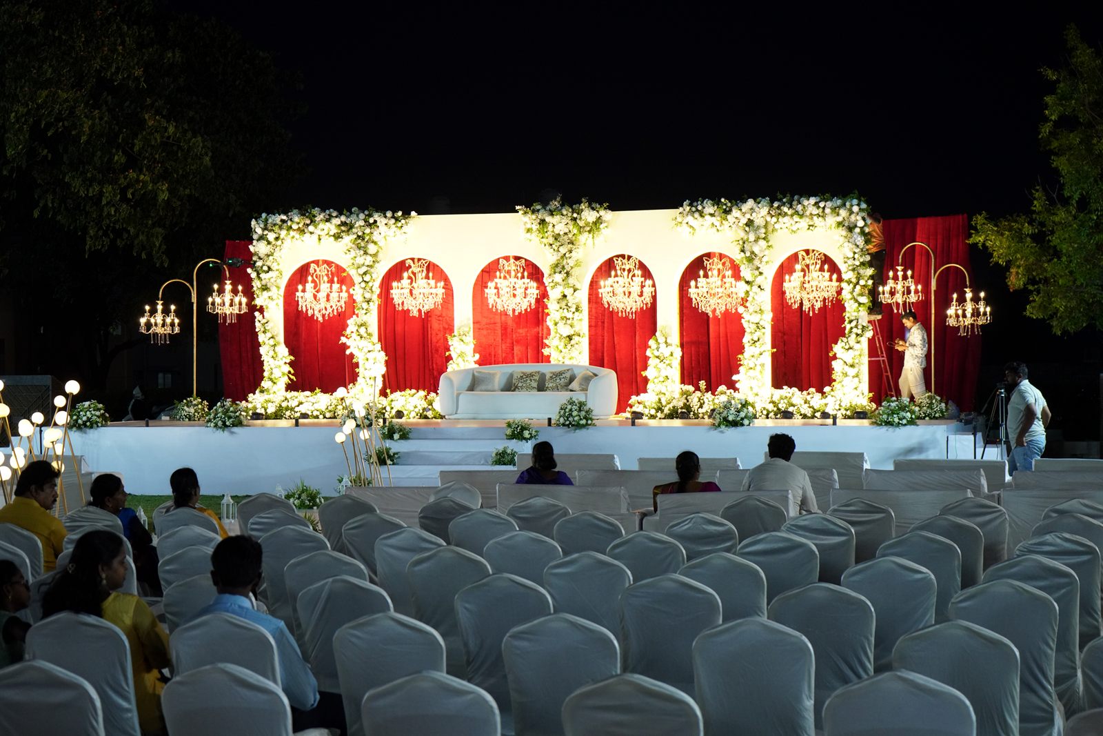 Evening reception stage with red and white floral arches and chandeliers at Sachin and Sharon’s wedding