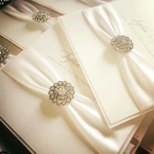 Ivory wedding invitations with satin ribbon wraps and crystal brooch details